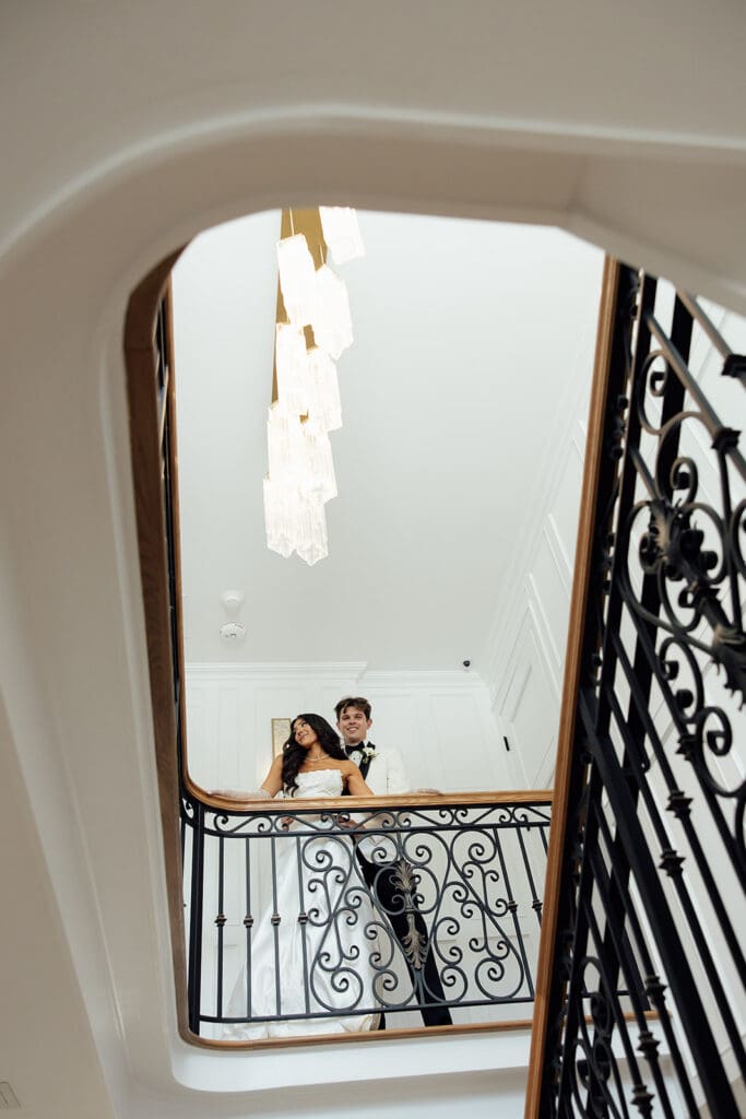 Shot from below of a bride and groom posing against the railing inside the The English Manor in Ocean, New Jersey. 